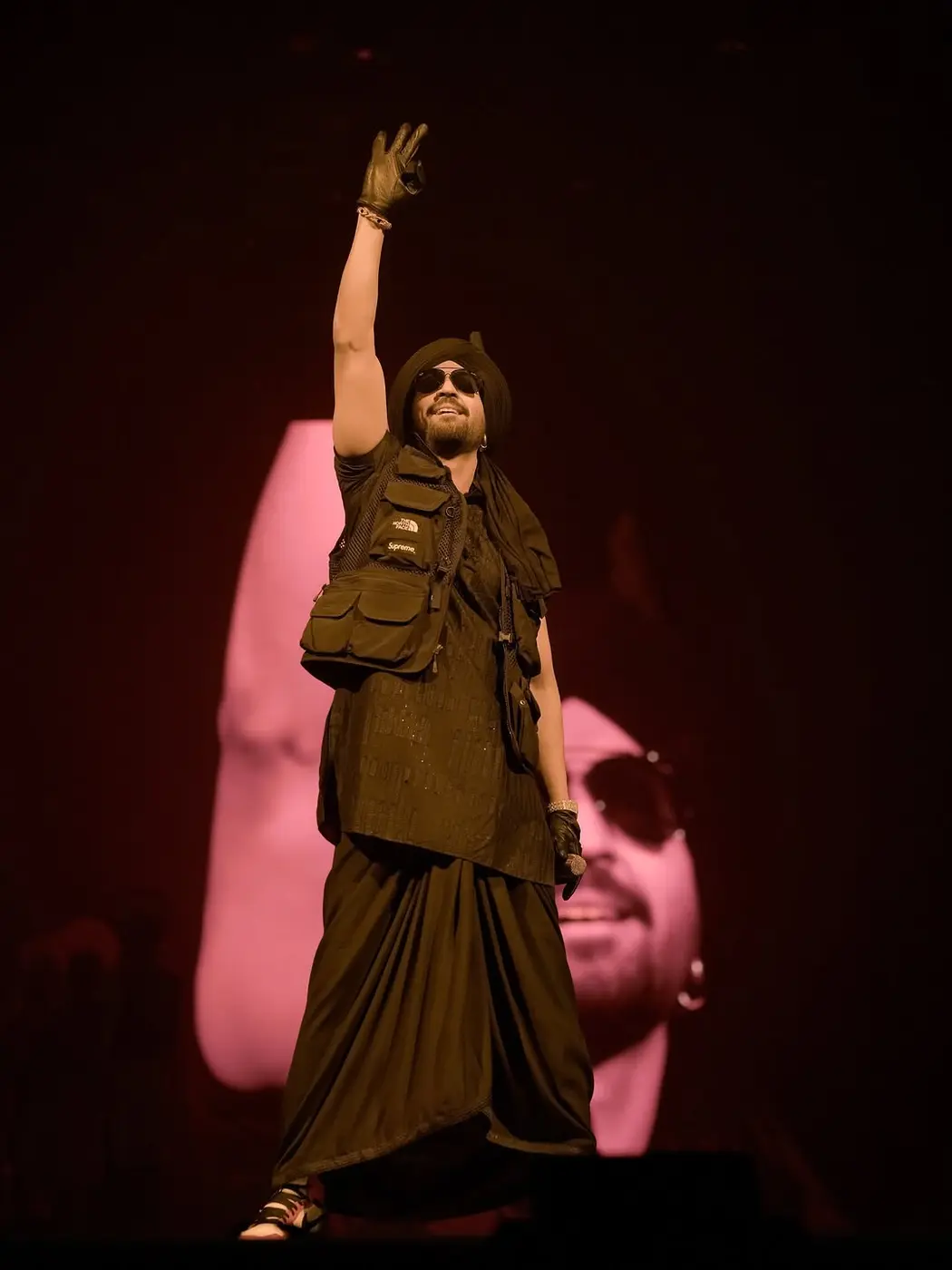 A headliner in a hat raising his arm under pink stage lights